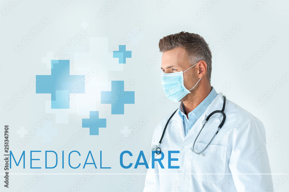 handsome doctor in medical mask looking away isolated on white with medical care lettering handsome doctor in medical mask looking away isolated on white with medical care lettering