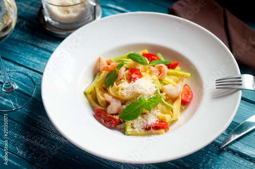 Fettuccini pasta with shrimps, tomato, avocado and grated parmesan cheese on wooden blue background, traditional Italian seafood dish