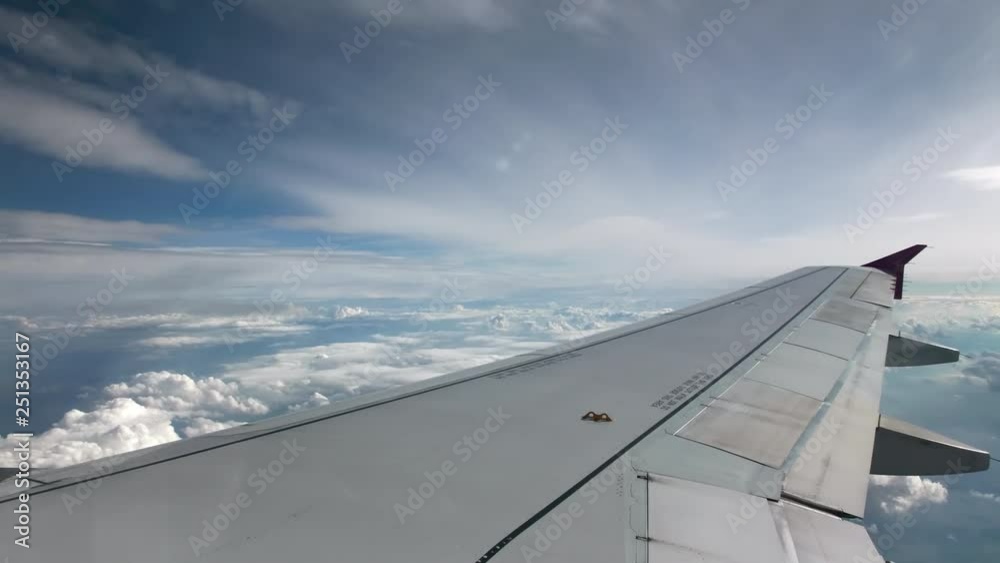 Flight of the plane on a flight level, against the background of blue sky and textural volumetric clouds. Rare clouds from above. View from the cockpit, in the foreground a gray wing of an airliner Flight of the plane on a flight level, against the background of blue sky and textural volumetric clouds. Rare clouds from above. View from the cockpit, in the foreground a gray wing of an airliner