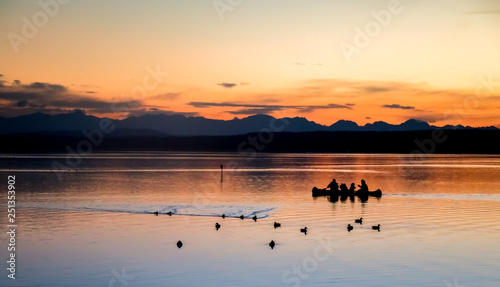 family in kayak at orange sunset, dark silhouette in the lake 