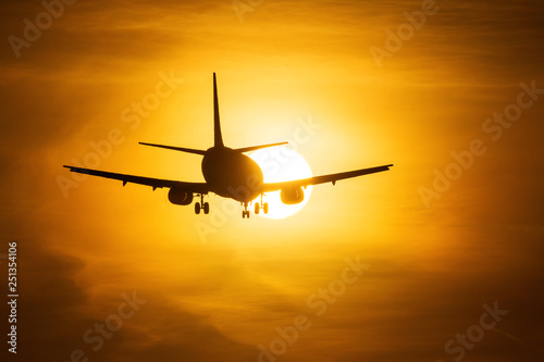 Silhouette of an air plane over the sun with beautiful red clouds in background