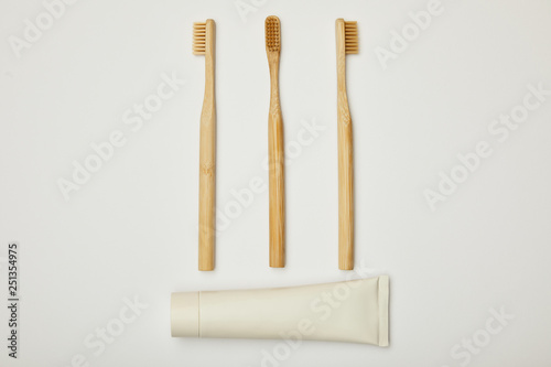 top view of toothpaste in tube and bamboo toothbrushes on white background