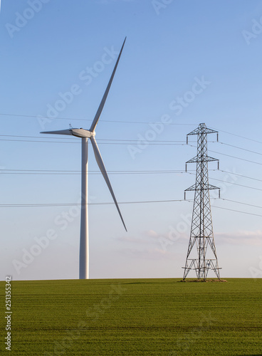 Wind turbine and electricity pylon in green field on blue sky