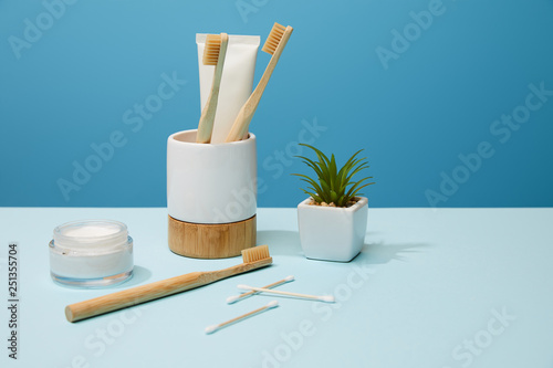 holder for toothbrushes, cosmetic cream and plant in pot on table and blue background