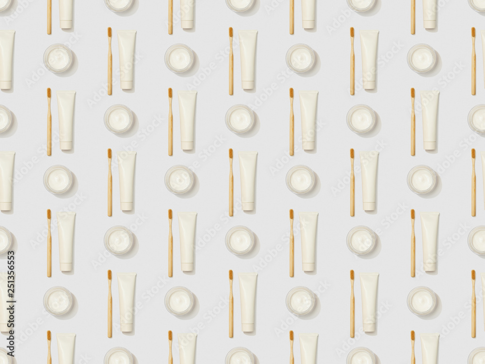 vertically bamboo toothbrushes, toothpaste in tube and cosmetic cream on grey background, seamless background pattern