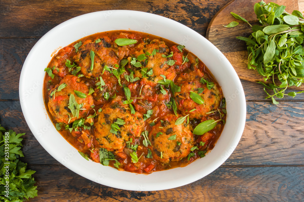 Chopped fish cutlets in spicy tomato sauce with fresh mint. White dish on wooden rustic table, top view