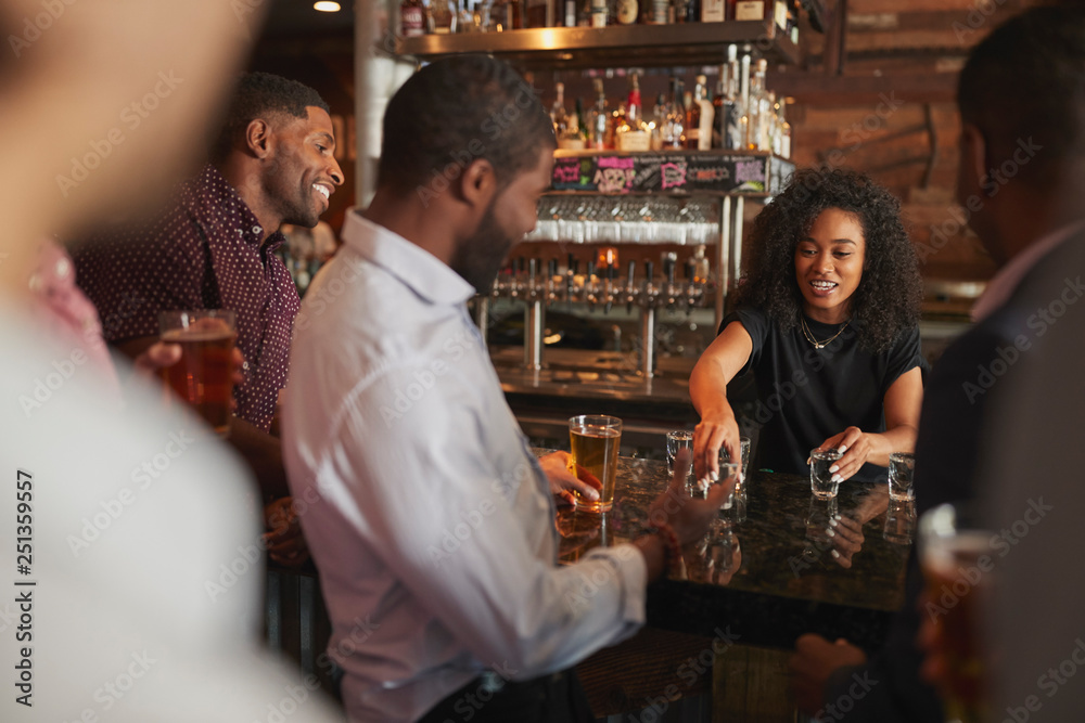 Barmaid Serving Shots To Group Of Male Friends On Night Out In Bar
