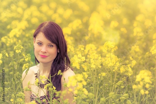 Happy summer love woman sitting down in rapeseed field smiling. Attractive young beauty girl enjoying the warm sunny sun in nature takes time feeling sustainability contemplation and youth wellbeing