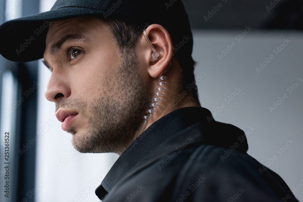 close up of handsome guard in black uniform with earphone looking away close up of handsome guard in black uniform with earphone looking away