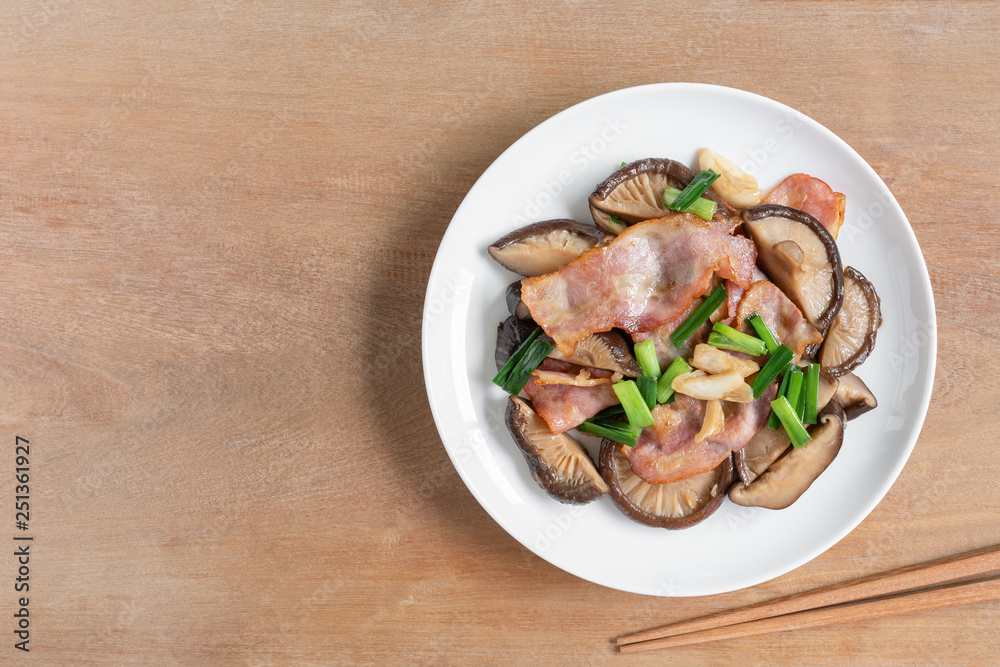 top view of stir fried shiitake mushroom and bacon with soy sauce in a ceramic dish on wooden table. homemade style food concept. top view of stir fried shiitake mushroom and bacon with soy sauce in a ceramic dish on wooden table. homemade style food concept.
