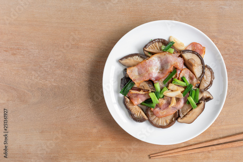 top view of stir fried shiitake mushroom and bacon with soy sauce in a ceramic dish on wooden table. homemade style food concept.