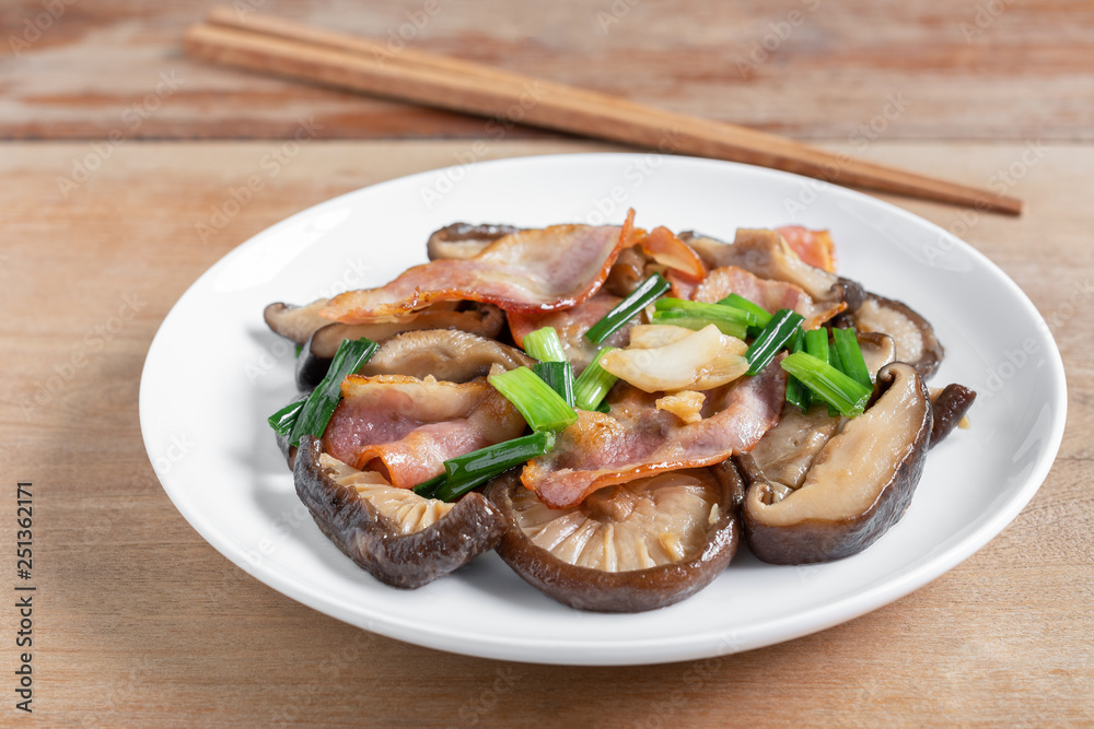 stir fried shiitake mushroom and bacon with soy sauce in a ceramic dish on wooden table, close up. homemade style food concept. stir fried shiitake mushroom and bacon with soy sauce in a ceramic dish on wooden table, close up. homemade style food concept.