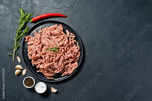Raw ground beef on a stone Board. Ingredients for cooking, rosemary, chili pepper, garlic, salt. Black background, top view, space for text