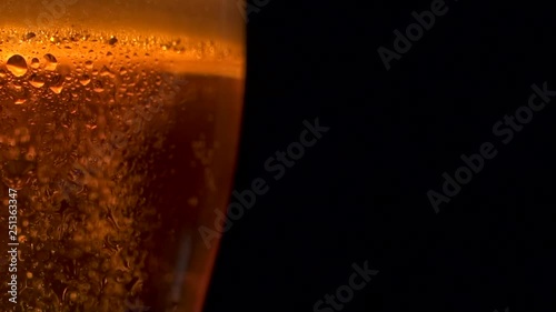 Close-up rising up many air golden bubbles of cooled beer in big glass with water drops. Refreshing alcohol beverage with white fluffy foam isolated at black background slowmo