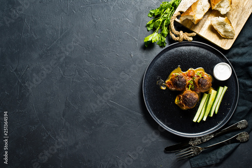 Swedish meatballs in tomato sauce on a black plate, cucumbers, salt, bread. Black background, top view, space for text