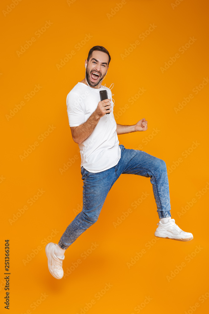 Photo of emotional man 30s singing while using earphones and mobile phone, isolated over yellow background Photo of emotional man 30s singing while using earphones and mobile phone, isolated over yellow background