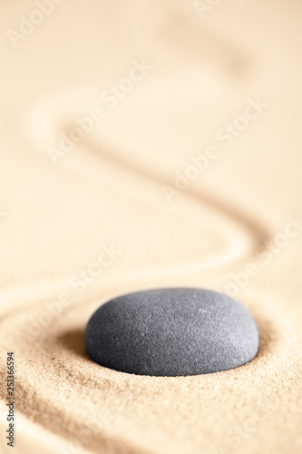Zen meditation stone for concentration and relaxation giving energy and inspiration. Concept for balance, harmony hope and purity. Round rock on textured sand background with room for copy space.