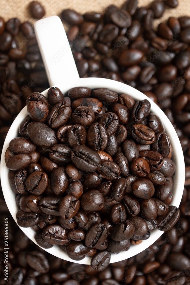 Fototapeta premium Many coffee beans in a cup of coffee on sackcloth. Top view focus.