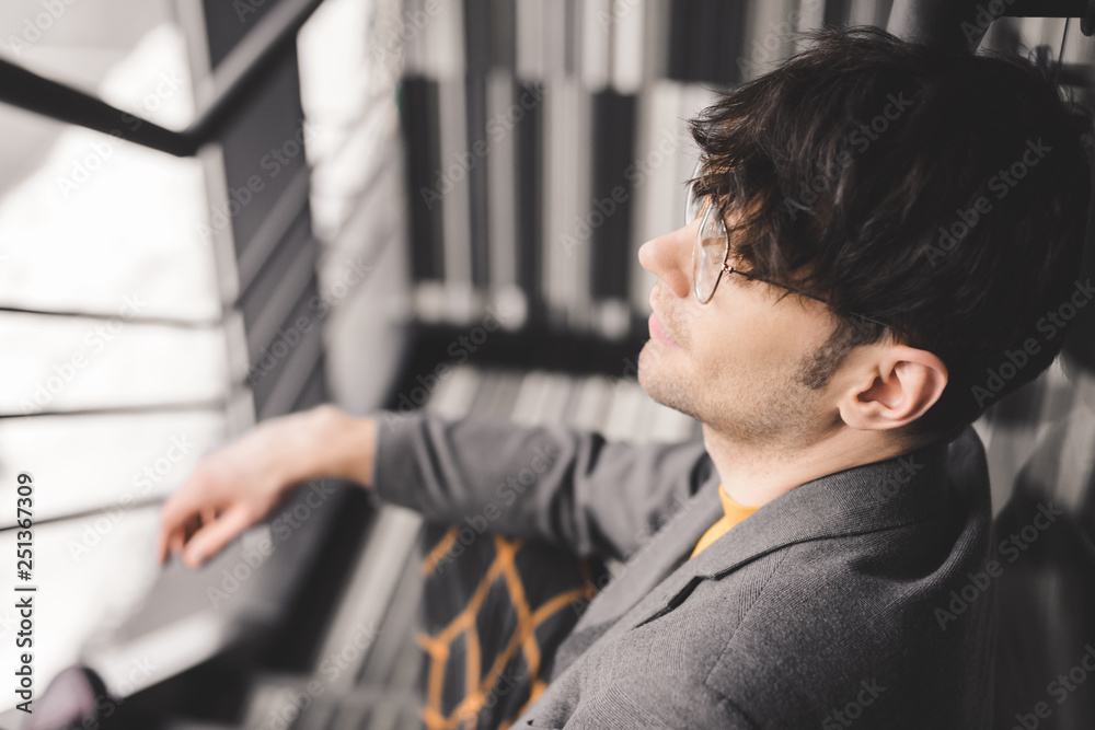 Obraz premium selective focus of dreamy young man in glasses sitting on stairs