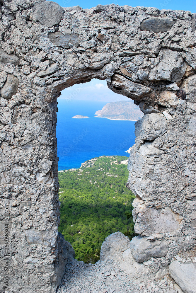 View of the coast through a window in the stone wall of the ruins of the Monolitos castle on the background of the coast, the island of Rhodes, Greece