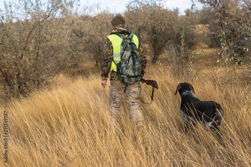 Hunter with a gun and a dog go on the first snow in the steppe  Hunting pheasant in a reflective vest 