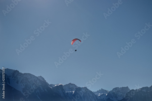 Paraglider tandem flying over alpine mountains.