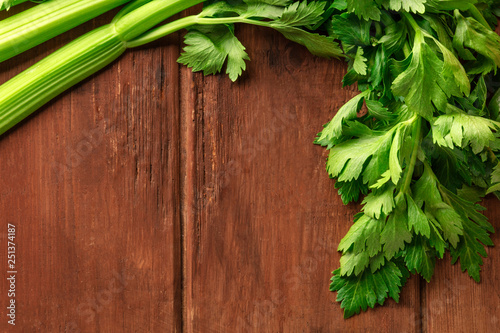 A closeup photo of fresh organic celery leaves and stalks, shot from the top on a dark rustic wooden background