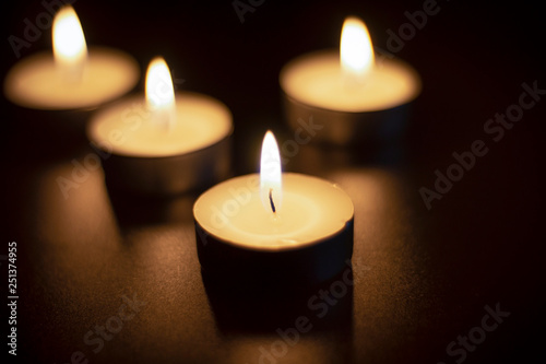 Four tea candles with reflection on black