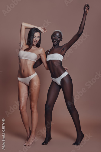 Wallpaper Mural Feeling playful. Full length of two attractive mixed race women looking at camera and smiling while standing against brown background Torontodigital.ca