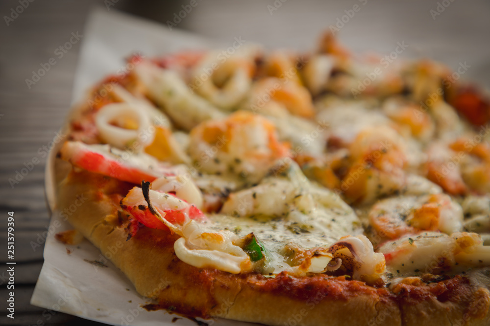 Baked small size homemade supreme seafood pizza on wooden table, close up Baked small size homemade supreme seafood pizza on wooden table, close up