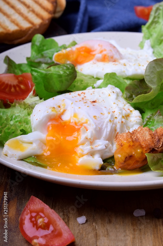 Poached egg with liquid yolk and green salad on a white plate