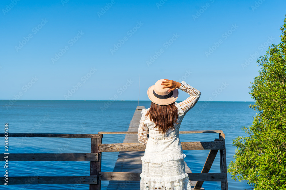 Women in a white dress, wearing a hat, looking forward to the beautiful scenery of the sky and the blue sea.