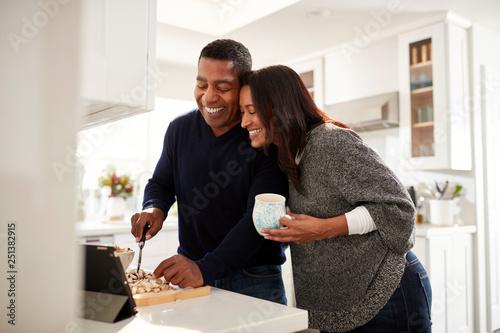 Картината върху платно Middle aged mixed race couple standing at worktop in the kitchen preparing food