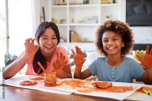 Two girlfriends having fun playing with modelling clay at home  smiling and showing dirty hands to camera  front view  close up