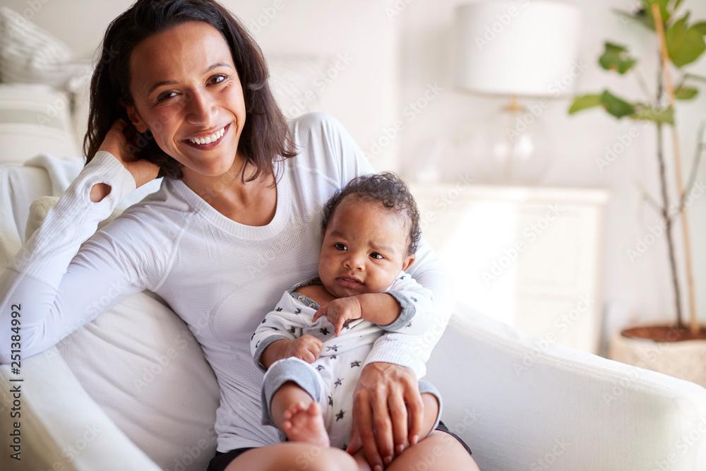 Happy mixed race young adult mother sitting on an armchair holding her three month old baby son, smiling to camera, close up Happy mixed race young adult mother sitting on an armchair holding her three month old baby son, smiling to camera, close up