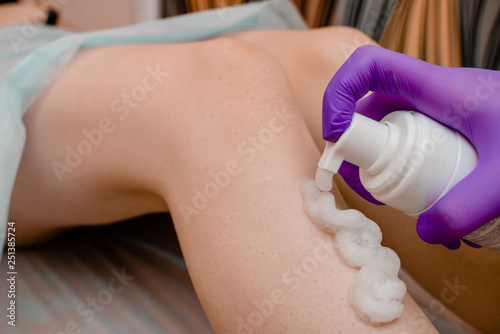 depilation and beauty concept - sugar paste or wax honey for hair removing with black gloves hands of cosmetologist in spa salon