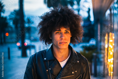 Serious looking young afro american man illuminated by showcase light in the street