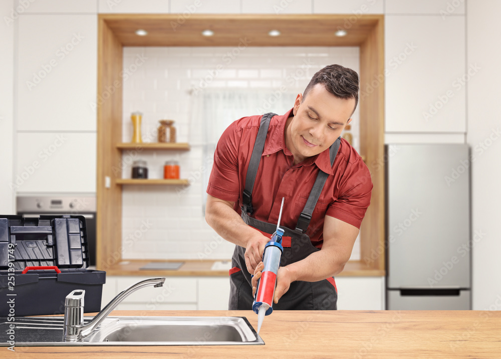 Plumber using a silicone tube on a sink inside a modern kitchen Plumber using a silicone tube on a sink inside a modern kitchen