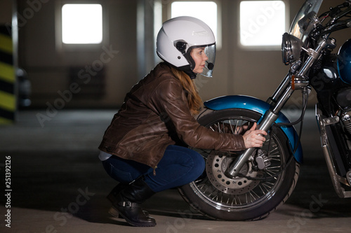 Woman motorcyclist sitting opposite wheel of chopper bike, making inspection before riding