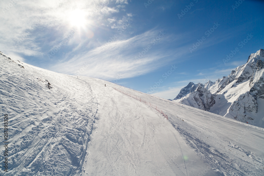 Snowboarder rides on a wide ski track on background of bright sun and the beautiful Caucasus Mountains