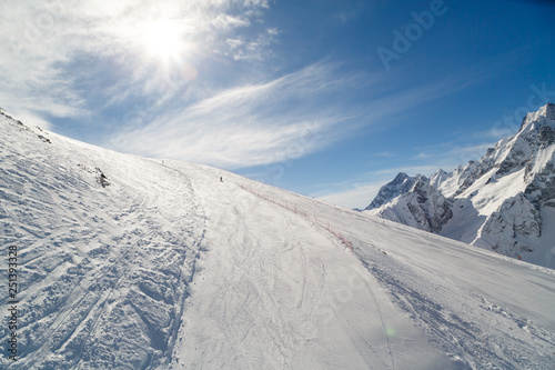 Snowboarder rides on a wide ski track on background of bright sun and the beautiful Caucasus Mountains © ovbelov1972