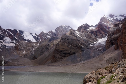 A mountain lake with grey water, surrounded by snow covered peaks, Lake Mutnoe, Fann Mountains, Tajikistan