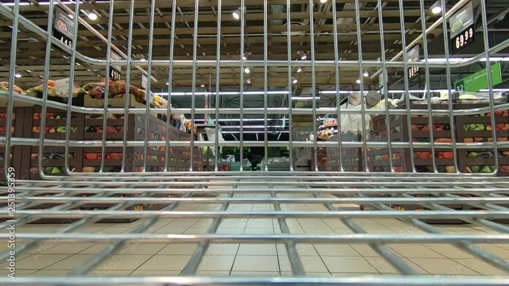 Buyer with a cart in the mall. Shopping arcade in a supermarket with household goods and food. Trolley close-up. Mall Background Buyer with a cart in the mall. Shopping arcade in a supermarket with household goods and food. Trolley close-up. Mall Background