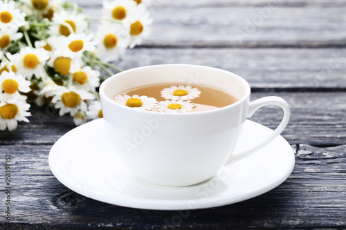 Cup of tea with chamomile flowers on grey wooden table