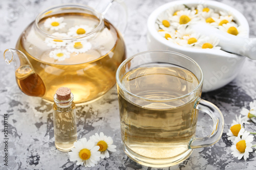 Cup of tea with oil in bottle and chamomile flowers on grey background