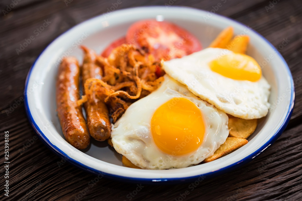 Typial breakfast with eggs, tomato, onion rings and sausage on plate Typial breakfast with eggs, tomato, onion rings and sausage on plate