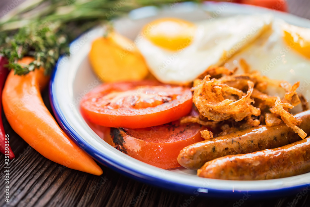 Typial breakfast with eggs, tomato, onion rings and sausage on plate Typial breakfast with eggs, tomato, onion rings and sausage on plate
