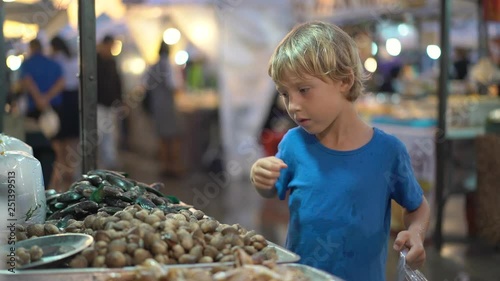 Slowmotion shot of a a little boy touching seashels on an Asian street market photo