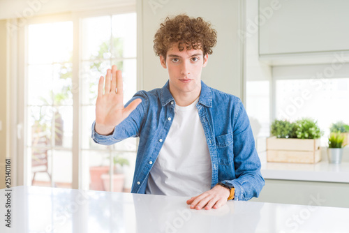 Young handsome man wearing casual denim jacket at home doing stop sing with palm of the hand. Warning expression with negative and serious gesture on the face. © Krakenimages.com