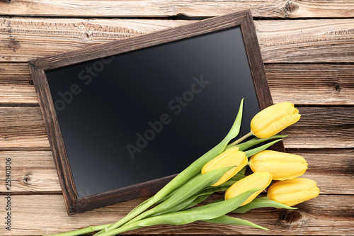 Bouquet of yellow tulips with blank frame on brown wooden table